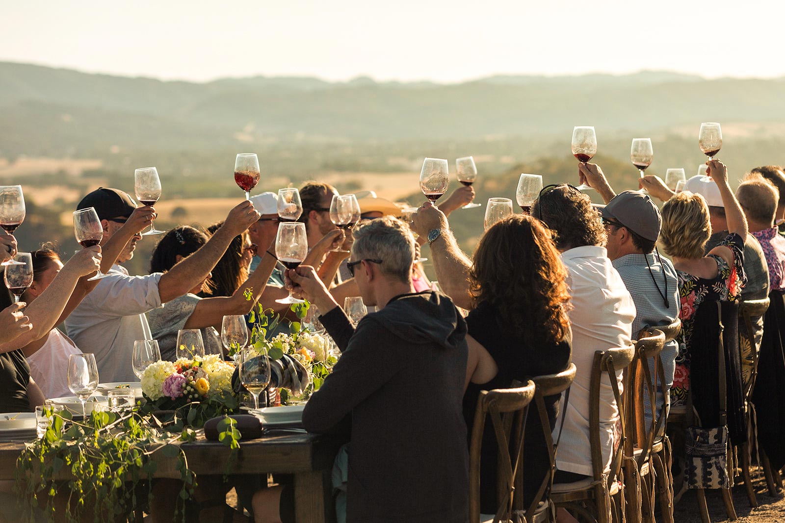 People sitting at a table at an outdoor event, toasting their wine glasses